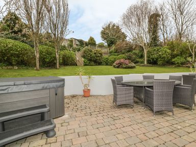 A patio area with a hot tub and outdoor dining table with chairs surrounded by a garden at The Orchard in Crantock