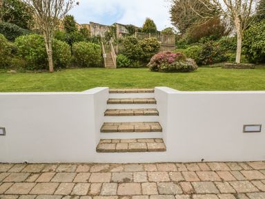 An outdoor garden with stone steps leading up to a grassy area with bushes and trees at The Orchard in Crantock
