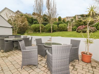 An outdoor patio with wicker chairs and glass tables overlooking a garden with stairs at The Orchard in Crantock
