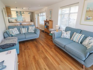 A living room with blue sofas and cushions next to a kitchen with a dining table at Kittiwake in Crantock