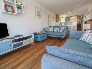 A living room with blue sofas and a TV unit with a television at Kittiwake in Crantock