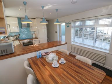 A kitchen with wooden countertops blue backsplash three hanging lights a dining table with tea set and white chairs at Kittiwake in Crantock