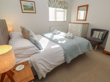 A bedroom with a double bed a bedside table with lamp a chest of drawers and a gray upholstered chair at Kittiwake in Crantock