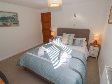A bedroom with a double bed with blue bedding two bedside tables with lamps and a framed painting on the wall at Kittiwake in Crantock