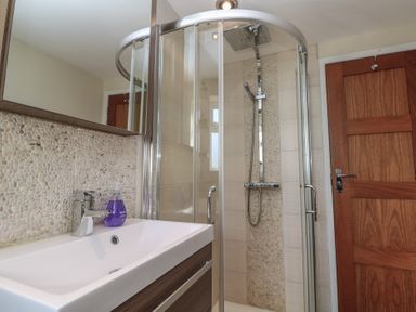 A bathroom with a sink and a liquid soap dispenser next to a curved glass shower cabin at Kittiwake in Crantock