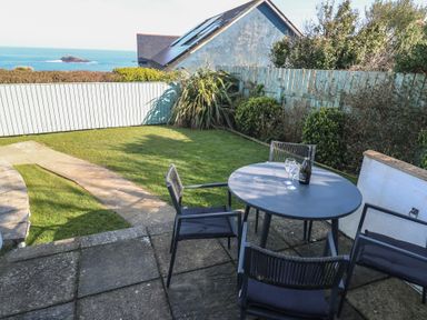 A garden with a round table and four chairs on a patio overlooking the sea at Kittiwake in Crantock