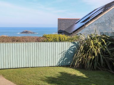 A fenced garden with grass and plants overlooking the sea with a small rocky island at Kittiwake in Crantock