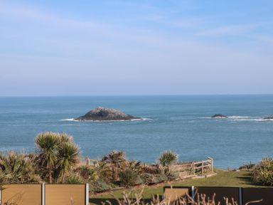 A coastal view with rocks in the sea and vegetation near a fence at Kittiwake in Crantock