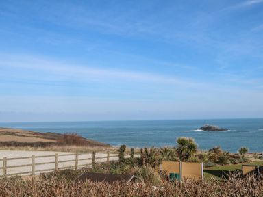 A coastal view with a wooden fence grassy area and an island in the sea at Kittiwake in Crantock
