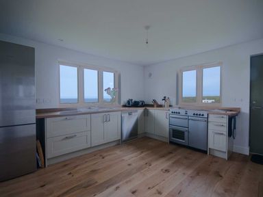 A kitchen with cabinets a refrigerator dishwasher stove sink and two windows at Kareena in Crantock