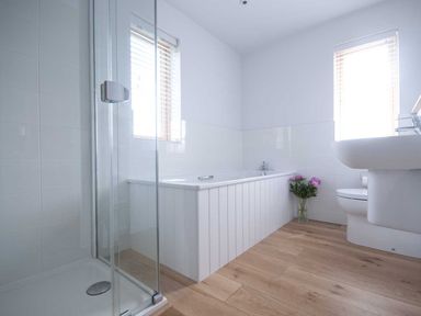 A bathroom with a shower enclosure bathtub toilet and sink with flowers on the floor by the bathtub at Kareena in Crantock