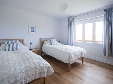 A bedroom with two single beds white bedspreads striped pillows a wooden floor a window with striped curtains at Kareena in Crantock