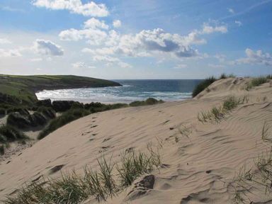 A sandy beach with grass patches and footprints overlooking the ocean with a coastal headland in the distance at Kareena in Crantock