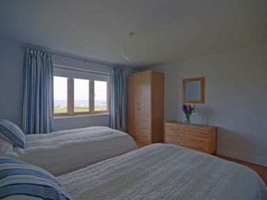 A bedroom with two beds a wooden wardrobe and dresser with a mirror and flowers by the window at Kareena in Crantock