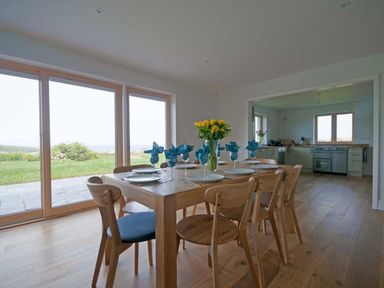 A dining room with a wooden table and chairs set with plates and glasses overlooking a garden at Kareena in Crantock