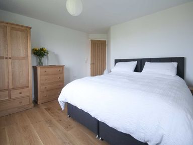 A bedroom with a double bed with white bedding wooden wardrobe and chest of drawers with flowers at Kareena in Crantock