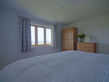 A bedroom with a bed a wooden wardrobe and dresser with flowers by a window at Kareena in Crantock