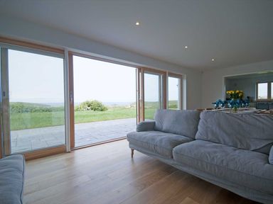 A living room with large sliding glass doors opening to a grassy outdoor area at Kareena in Crantock