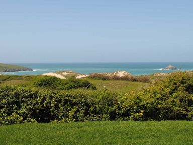 Green grass and bushes in front of sand dunes with the ocean and clear sky in the background at Kareena in Crantock