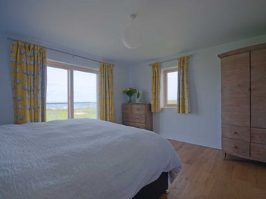 A bedroom with a large bed white bedding yellow curtains wooden dresser and wardrobe at Kareena in Crantock