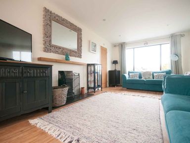 A living room with teal sofas a large window and a rug at Keelyn in Crantock