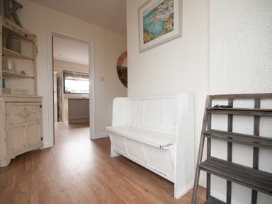 A hallway with a white wooden bench a wooden shelf a cabinet and a kitchen visible through a doorway at Keelyn in Crantock