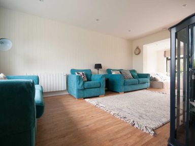 A living room with teal armchairs and sofa a floor lamp a wall clock and a light rug on wooden floor at Keelyn in Crantock