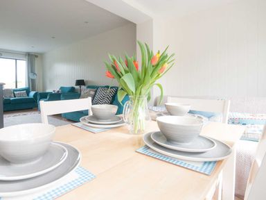 A dining table set with grey dishes and a vase of tulips next to a living room with blue sofas at Keelyn in Crantock