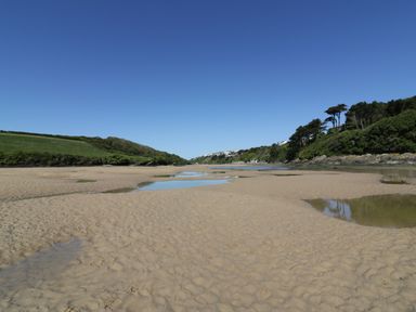 A sandy beach with small pools of water and green hills on both sides at Keelyn in Crantock