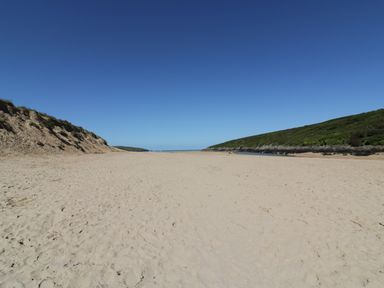 A sandy beach between two green hills under a clear blue sky at Keelyn in Crantock