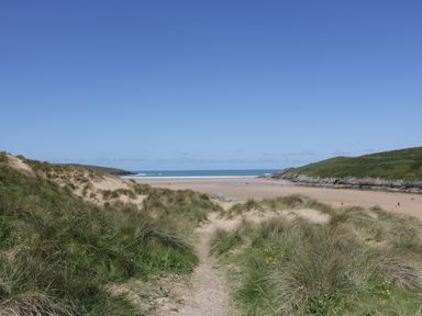 A sandy beach with grassy dunes leading to the ocean and hills on both sides at Keelyn in Crantock
