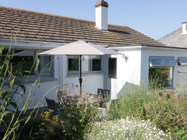 A patio area with a table umbrella and chairs surrounded by plants outside a white house with tiled roof at Keelyn in Crantock