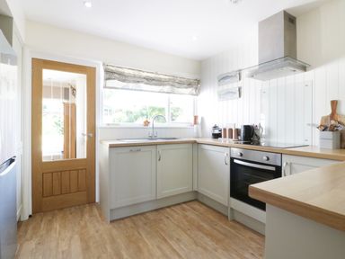A kitchen with wooden countertops a stainless steel oven a window with a patterned blind and a wooden door at Keelyn in Crantock