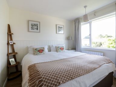 A bedroom with a double bed two crab pillows a brown patterned throw beside a window with curtains and a wooden corner shelf at Keelyn in Crantock