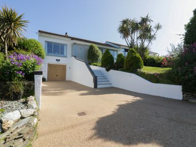 A driveway leading to a garage and stairs with a white wall and plants around the house at Keelyn in Crantock