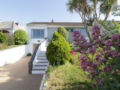 A bungalow with stairs leading to the entrance and a garden with green bushes and purple flowers at Keelyn in Crantock