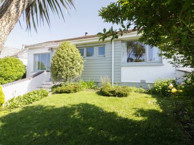 The front garden with lawn bushes and trees in front of a single story house at Keelyn in Crantock