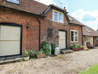 A brick house exterior with cream doors and windows a gravel pathway plants and milk churns at Downs View Dairy in West Tytherley