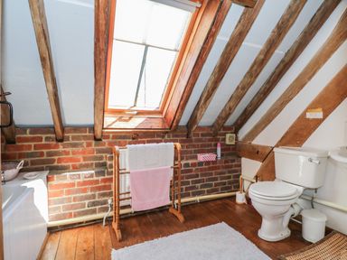 A bathroom with a toilet wooden towel rack wooden floor skylight window exposed wooden beams and brick wall at Downs View Dairy in West Tytherley