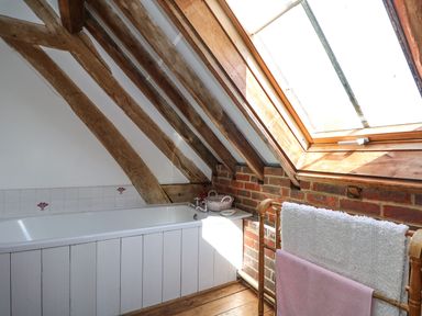 A bathroom with wooden beams a bathtub a towel rack and a skylight window at Downs View Dairy in West Tytherley