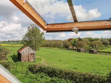 A view of a green field with a wooden shed and trees seen through an open skylight window at Downs View Dairy in West Tytherley