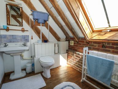 A bathroom with wooden beams a toilet a sink a mirror and a window at Downs View Dairy in West Tytherley