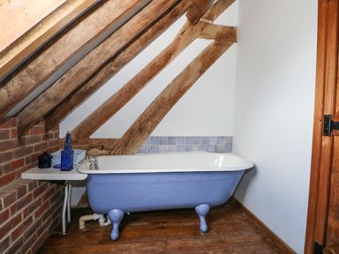 A bathroom with a blue clawfoot bathtub under a slanted wooden beam ceiling at Downs View Dairy in West Tytherley