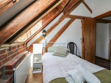 A bedroom with a single bed, wooden beams, a chair, radiator, and an open wooden door at Downs View Dairy in West Tytherley
