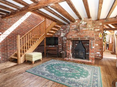 A living room with exposed brick walls wooden beams a staircase wood burning stove and a green patterned rug at Downs View Dairy West Tytherley