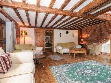 A living room with sofas armchair wooden beams and a patterned rug at Downs View Dairy in West Tytherley