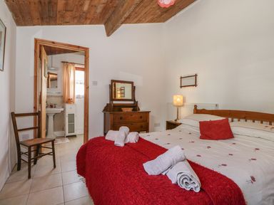 A bedroom with a double bed with red and white bedding a wooden chair a chest of drawers with a mirror and an open door leading to a bathroom at Downs View Dairy in West Tytherley