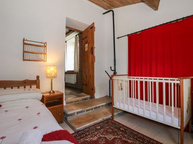 A bedroom with a single bed a bedside table with a lamp a crib and a door with steps at Downs View Dairy in West Tytherley