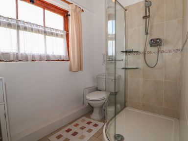 A bathroom with a window with curtains a toilet a corner shower with glass doors and a showerhead at Downs View Dairy in West Tytherley