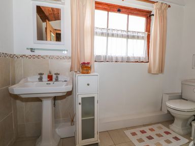 A bathroom with a pedestal sink toilet white cabinet window with curtains and a rug on the floor at Downs View Dairy in West Tytherley